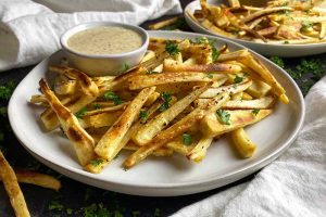 Horizontal image of fries on two white plates with a bowl of creamy dip next to white towels.