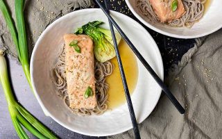 Horizontal image of white bowlfuls of a fish fillet on top of noodles and broth with chopsticks next to scallions.