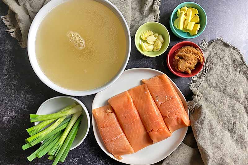 Horizontal image of raw fish fillets next to bowls of broth and seasonings.