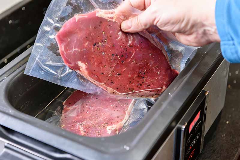 Horizontal image of a hand inserting a sealed piece of raw seasoned beef in a machine.