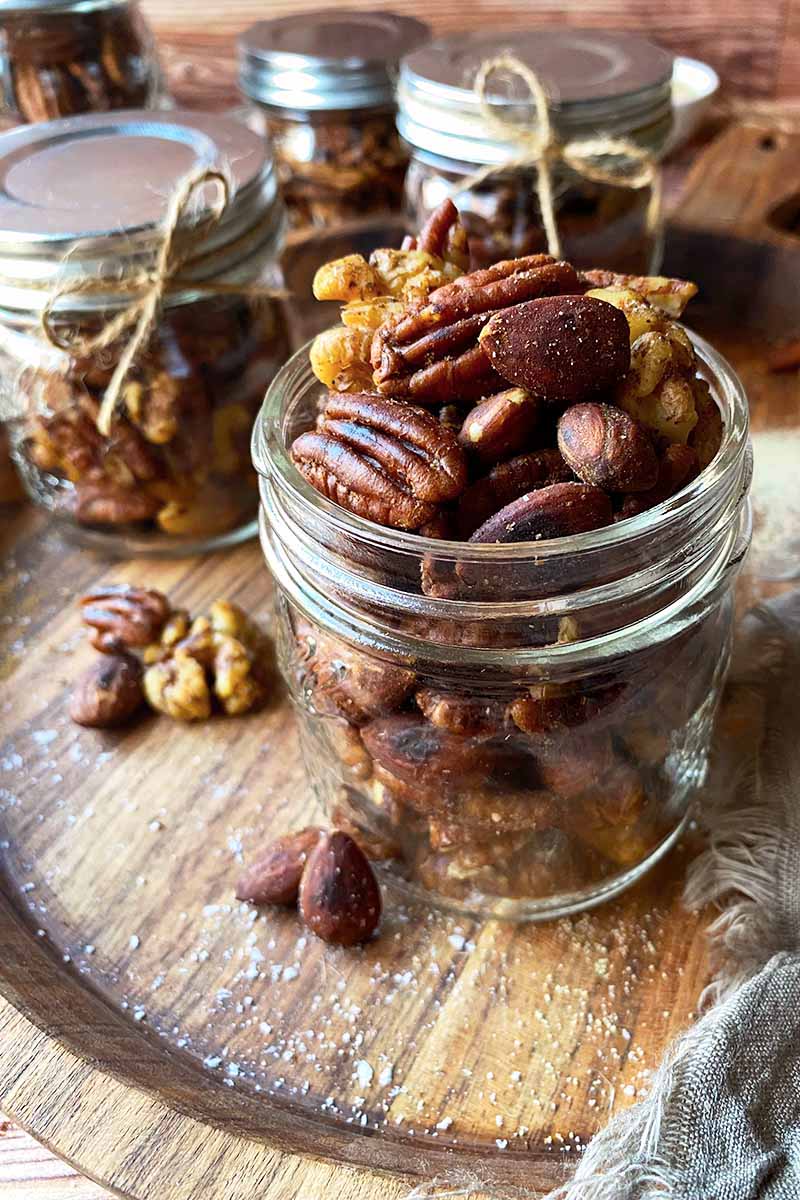 Vertical image of jars filled with a seasoned snack mix on a wooden cutting board.