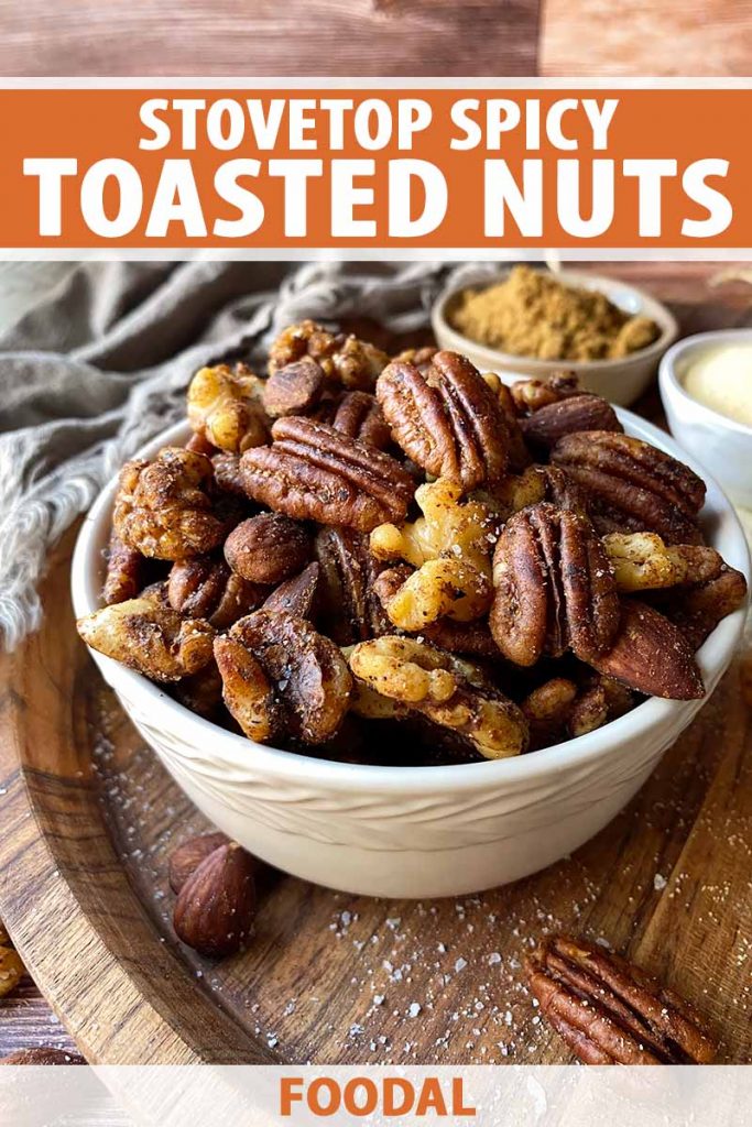 Vertical image of a white bowlful of seasoned pecans, walnuts, and almonds on a white board, with text on the top and bottom of the image.