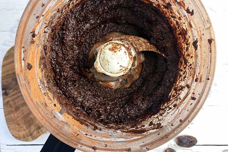 Horizontal image of a thick dark brown paste in a food processor.