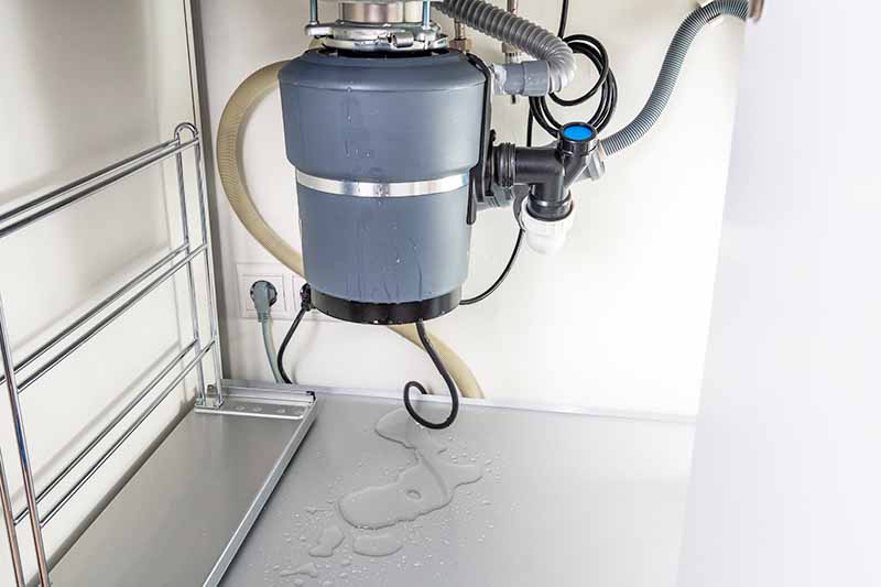 Horizontal image of a leaking kitchen equipment under a sink.
