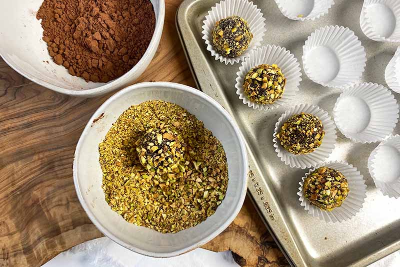 Horizontal image of coating balls in ground pistachios, putting them in cupcake liners on a pan.