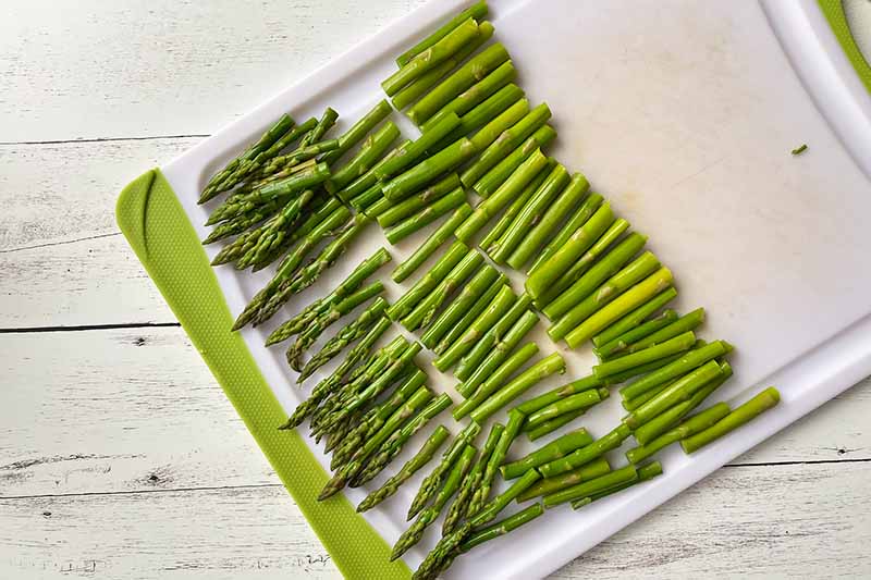 Horizontal image of sliced green vegetable stalks on a cutting board.