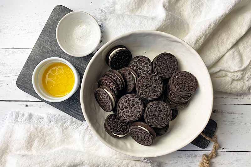 Horizontal image of Oreo cookies, melted butter, and salt in white bowls.