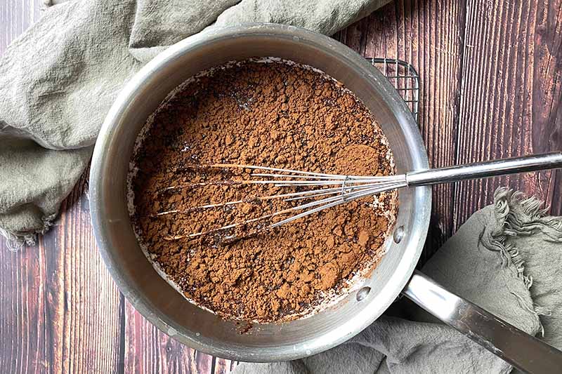 Horizontal image of whisking together cocoa powder in a milk mixture in a pot.