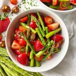 Horizontal image of two white bowls filled with a mix of green vegetables, strawberries, and tomatoes.