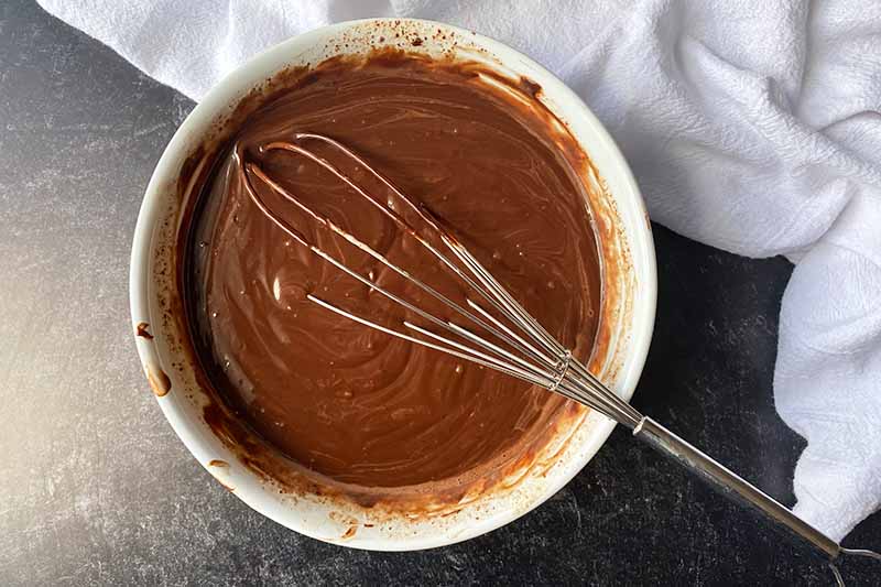 Horizontal image of whisking a dark brown creamy mixture together in a white bowl.