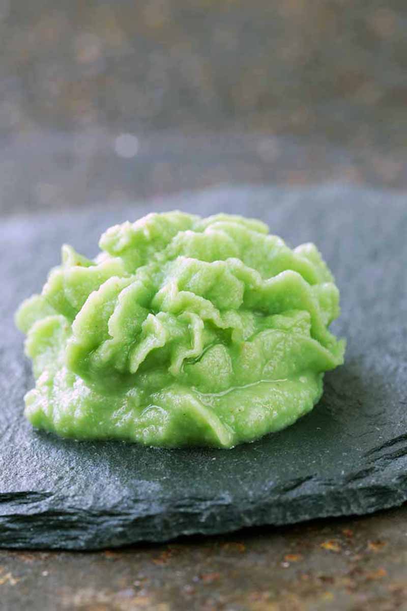Vertical image of a mound of a wet green condiment on a slate.