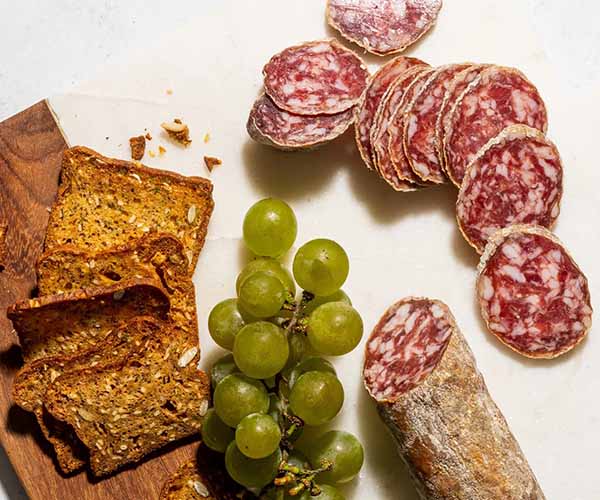 Image of the Smoking Goose Rust Belt Saucisson, sliced next to grapes and crackers.