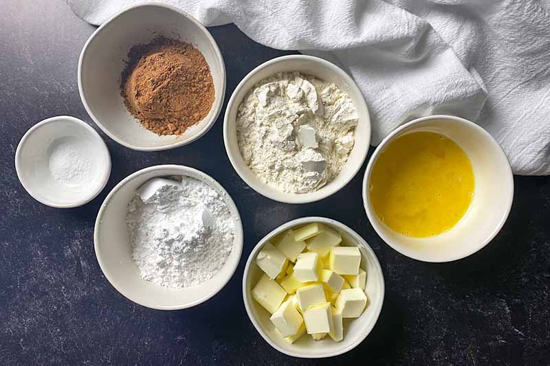 Horizontal image of assorted wet and dry ingredients prepped and measured in small white bowls.