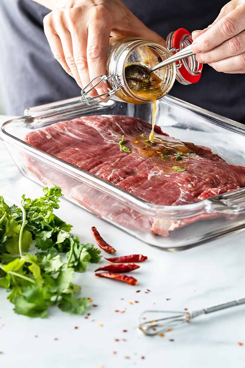 Vertical image of applying marinade on raw meat.