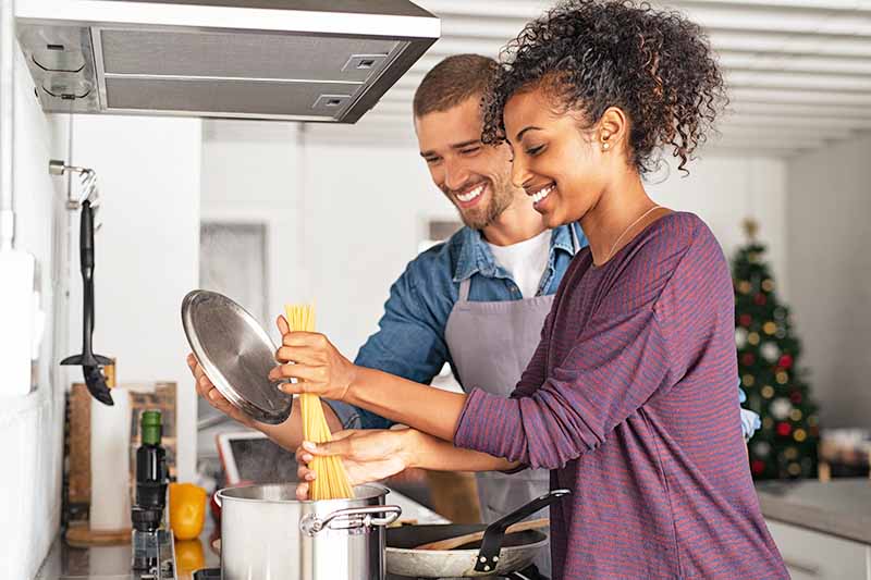 Horizontal image of a couple adding pasta to a pot of water.