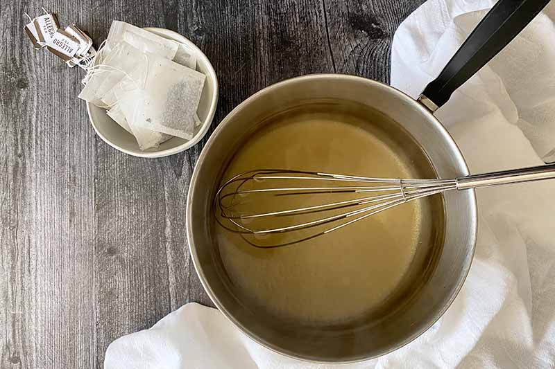 Horizontal image of a liquid in a pot with a whisk next to a bowl filled with small white bags.