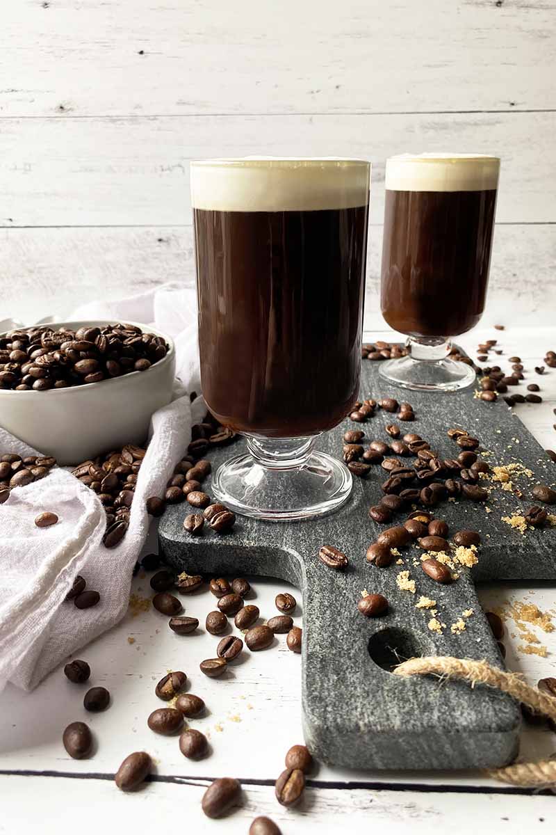 Vertical image of two mugs with a dark brown drink and fluffy white topping.