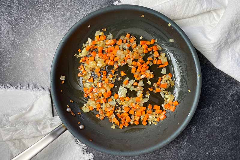 Horizontal image of cooking diced carrots and onions in a skillet.