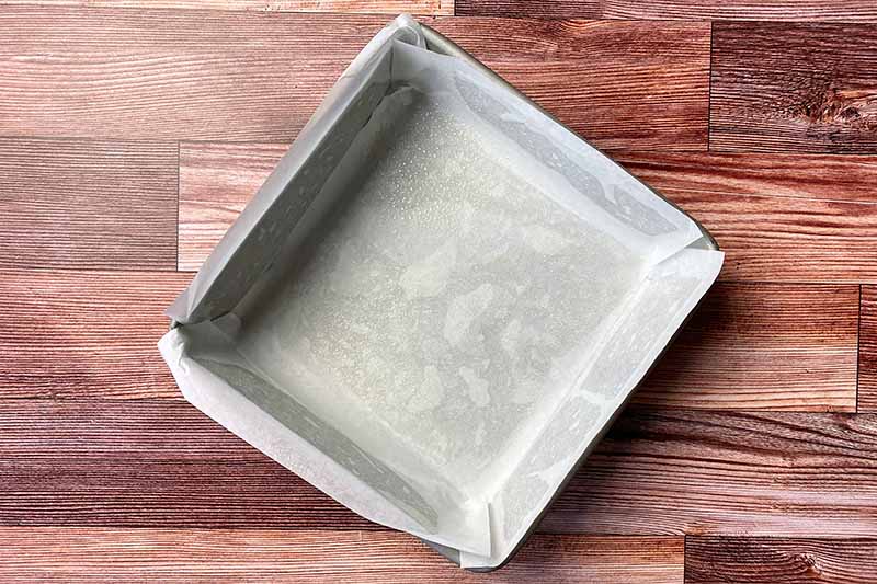 Horizontal image of a square metal pan greased and lined with parchment paper.