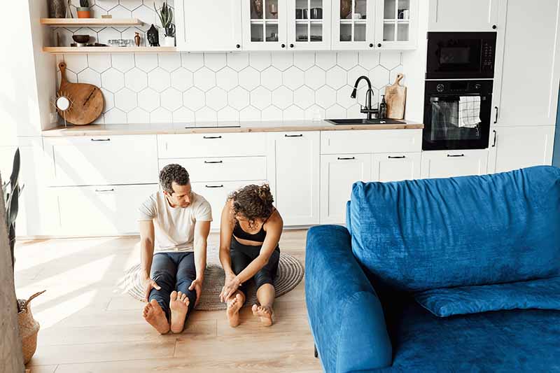 Horizontal image of a couple stretching together on the floor of their house.