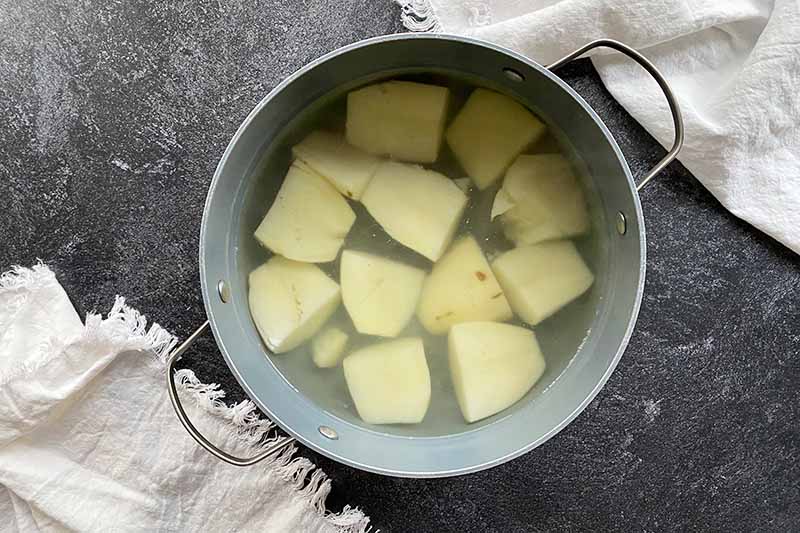 Horizontal image of a quartered white vegetable in water in a pot.