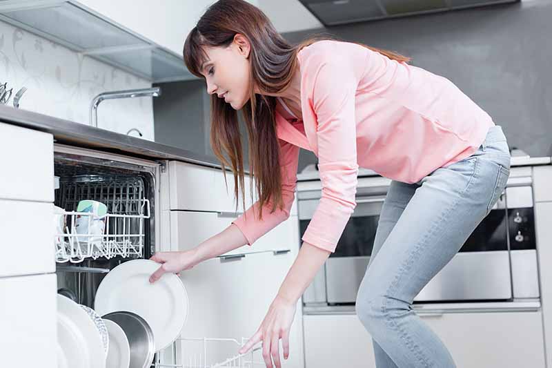 Horizontal image of a woman putting dishes in a dishwasher.