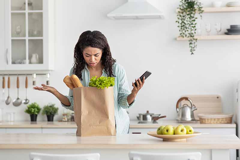 Horizontal image of a woman in distress looking inside a paper grocery bag with produce.