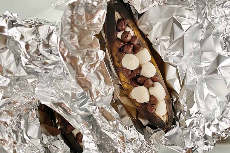 Horizontal image of puffy mini marshmallows and slightly melted candy chips stuffed in fruit wrapped in aluminum foil.