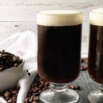 Horizontal image of two glasses filled with a dark brown beverage and whipped topping.