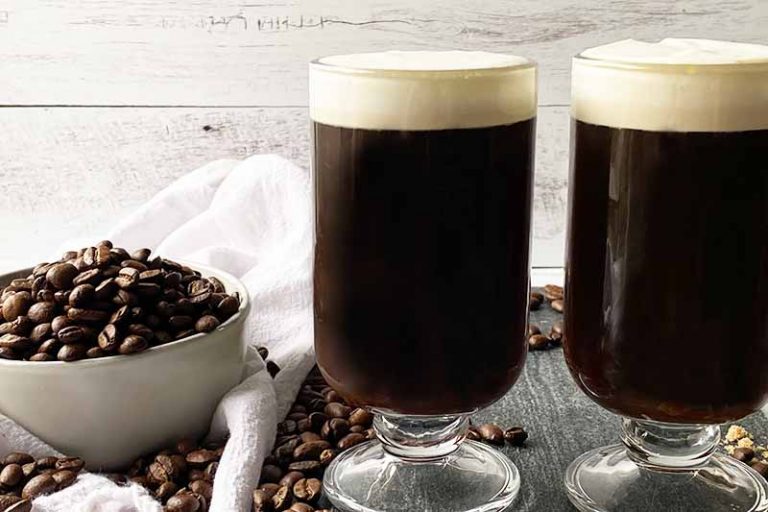 Horizontal image of two glasses filled with a dark brown beverage and whipped topping.