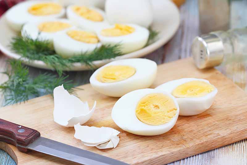 Horizontal image of peeled hard-boiled eggs on a wooden cutting board.
