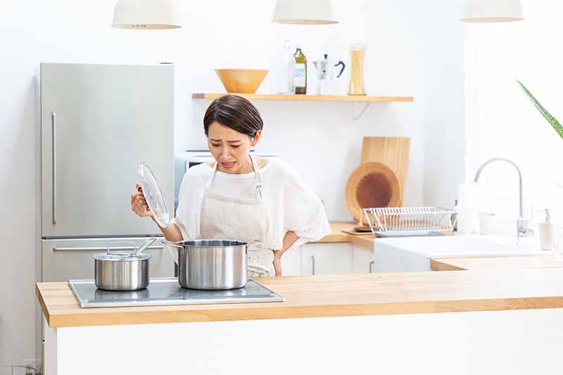 Horizontal image of a woman in distress looking into a pot on the stovetop.