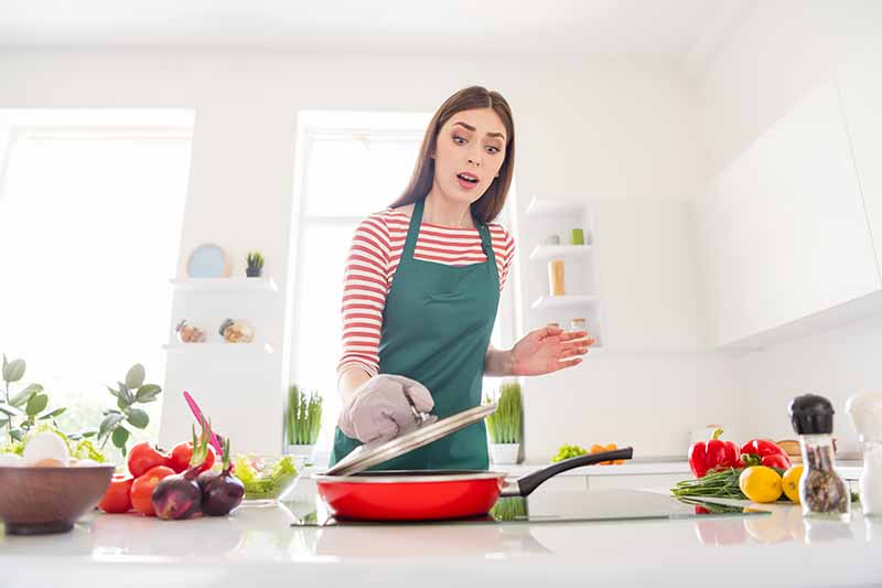 Horizontal image of a woman checking on food in a pan.