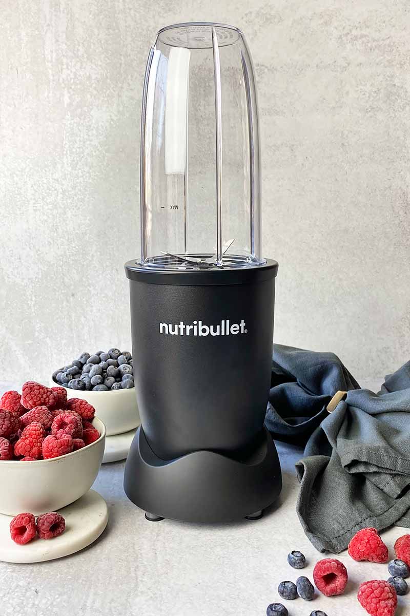 Vertical image of an personal-sized black blender next to bowls of fresh fruit.