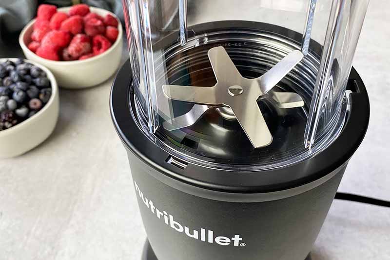 Horizontal image of an assembled personal blender appliance next to bowls of berries.