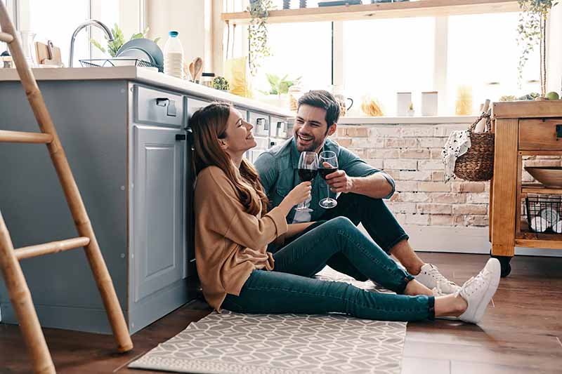 Horizontal image of a couple drinking wine while sitting on the kitchen floor.