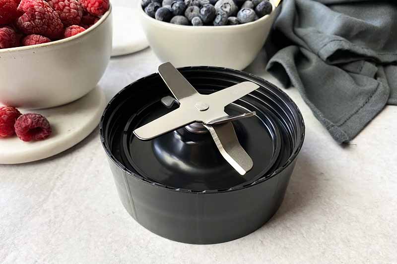 Horizontal image of an extractor blade next to bowls of raspberries and blueberries.