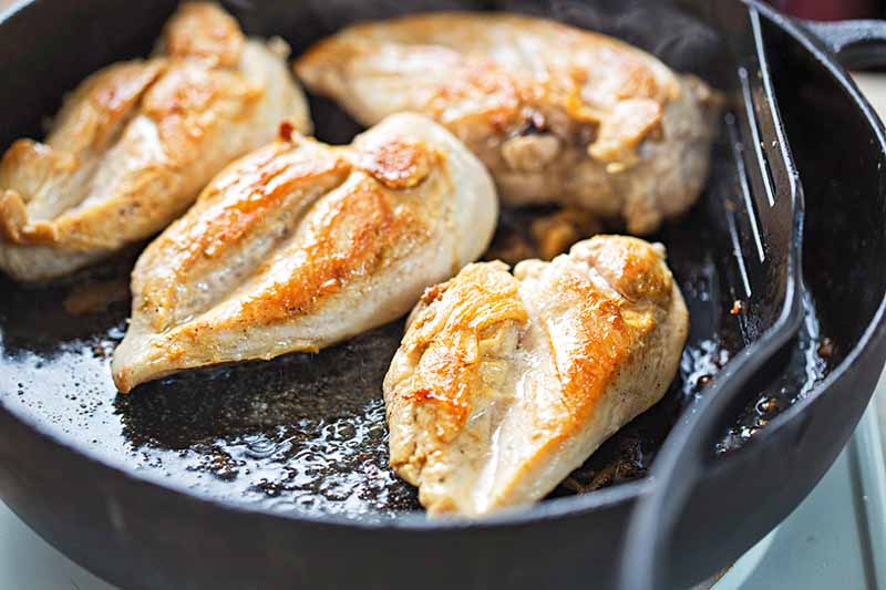 Horizontal image of searing pieces of chicken in a pan.