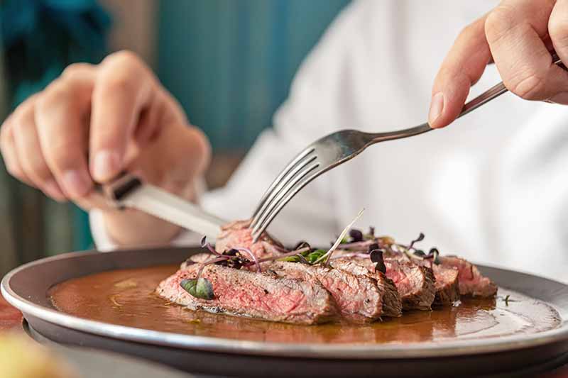 Horizontal image of slicing steak on a plate.