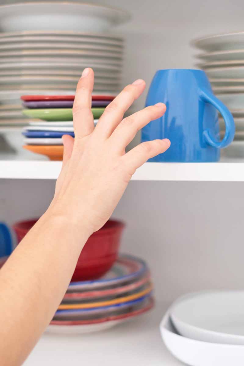 Vertical image of a hand reaching for a mug in a tall cabinet.