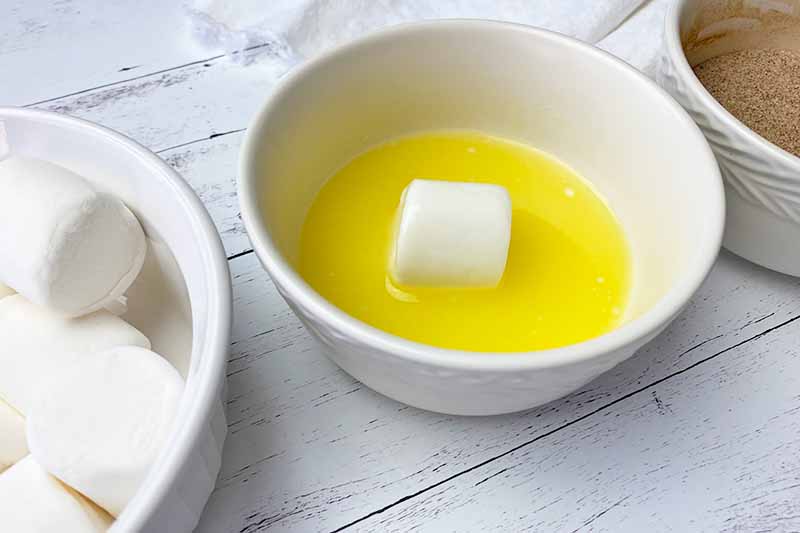 Horizontal image of coating a single marshmallow in melted butter in a bowl.