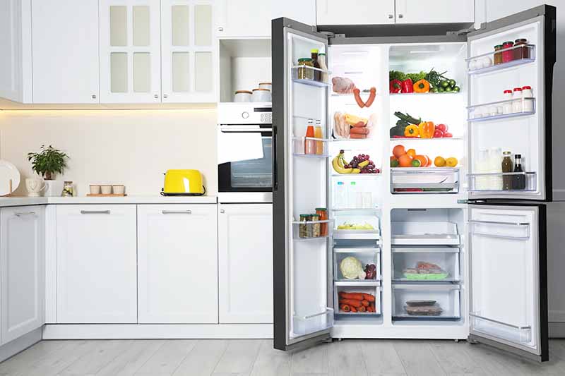 Horizontal image of an open fridge full of food in the kitchen.