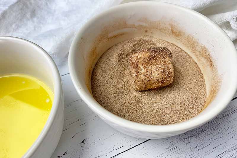 Horizontal image of coating a single marshmallow in cinnamon sugar in a bowl.