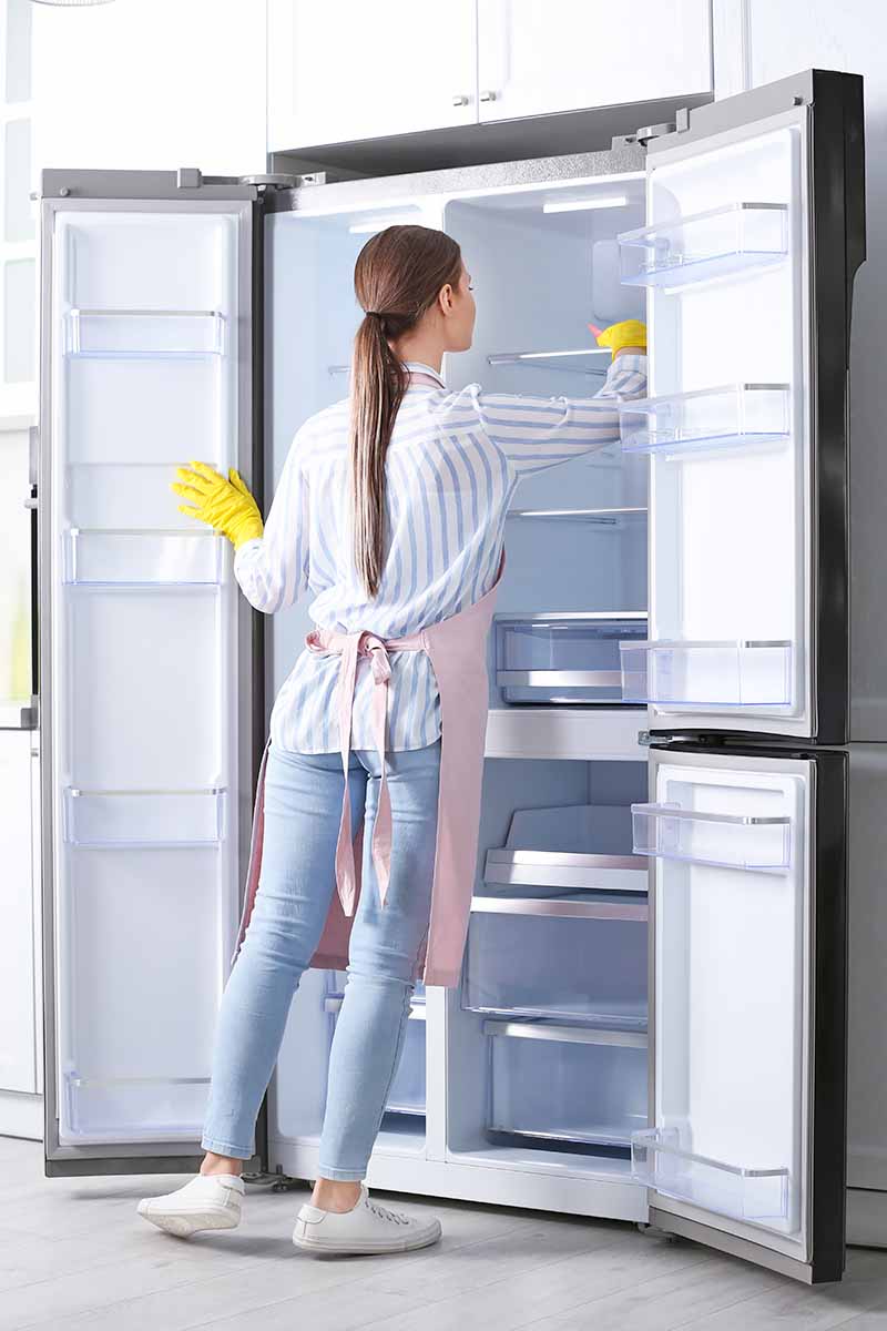 Vertical image of a woman cleaning her kitchen wearing yellow gloves.