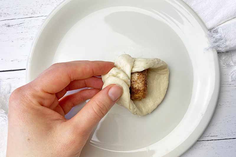 Horizontal image of covering a coated marshmallow in raw dough on a white plate.