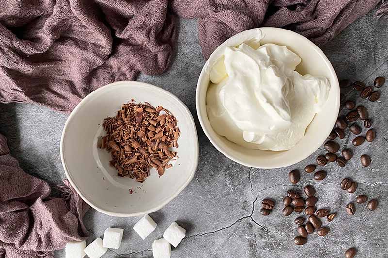 Horizontal image of whipped cream and shaved chocolate in white bowls.
