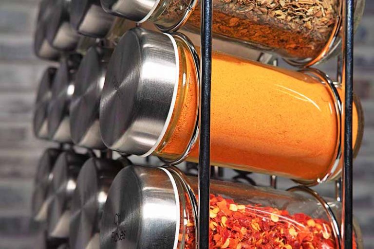 Horizontal close-up image of a metal organizer with rows of jarred seasonings with metal lids.