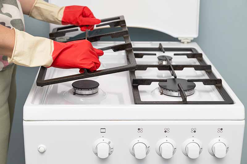 Horizontal image of gloved hands removing grates from a stovetop.