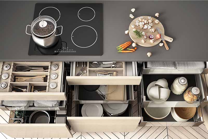 Horizontal image of multiple open drawers containing neatly arranged items, with a stovetop and prepped food on top.