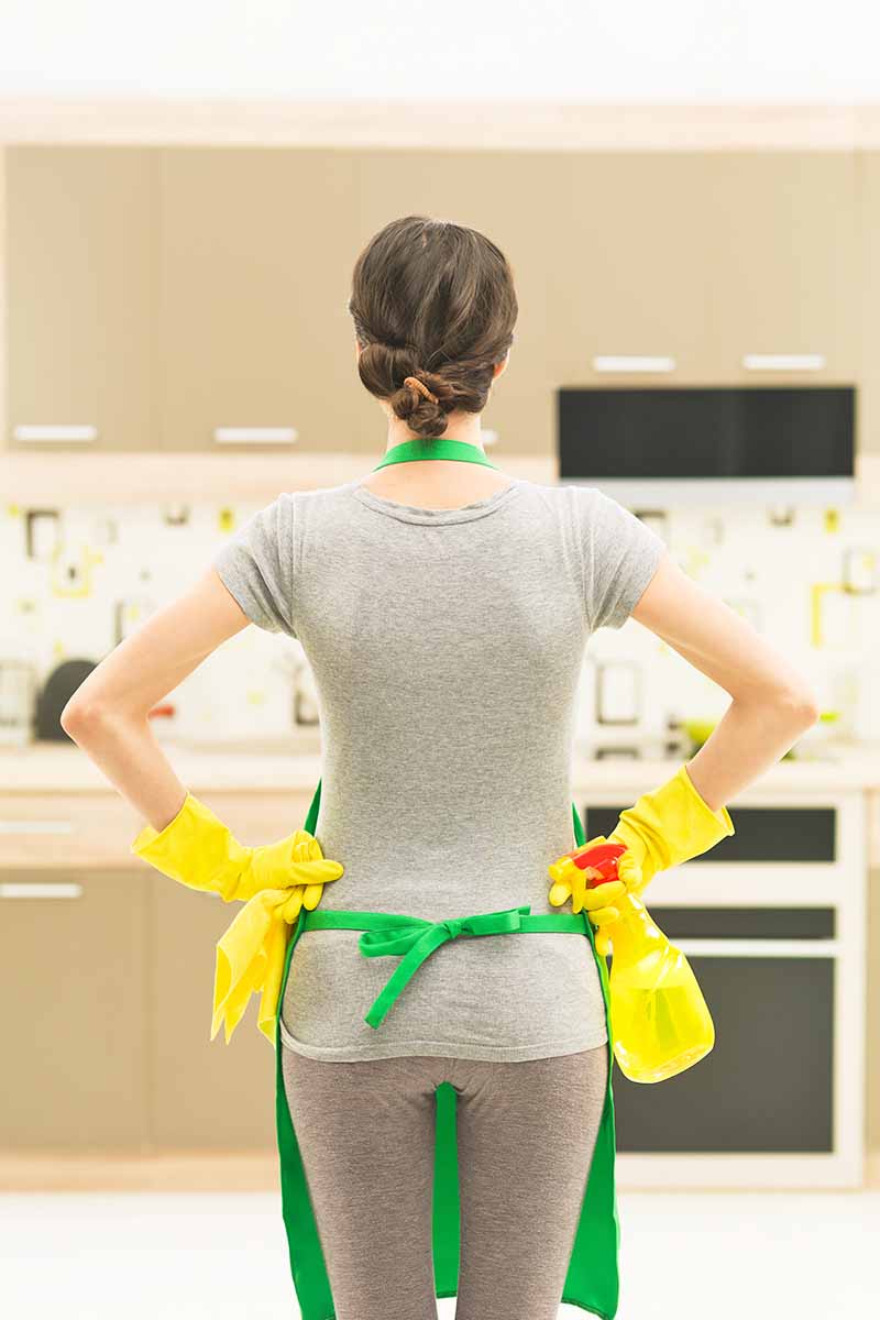 Vertical image of the back view of a woman standing while wearing an apron and yellow rubber gloves.